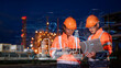 Double exposure Engineer team wear safety uniform stand hand holding tablet and laptop computer, survey inspection site with double hologram industry to work with night lights oil refinery background.