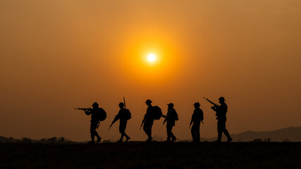 silhouette group of special forces sodiers walking and holding gun over the sunset and colorful orange sky background,