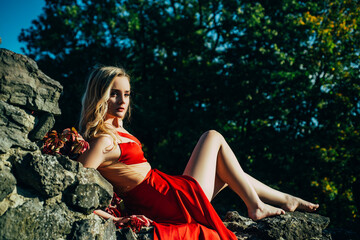 Woman, fashion model on fortress, old castle stones wall. Beautiful girl in stylish fashion red dress in summer. Fashion woman posing outdoors.