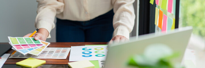 Poster - creative graphic designer holding color swatch to comparing color on document for designing project