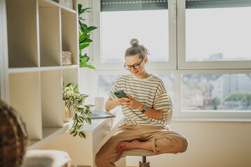 young adult caucasian woman in glasses working on a laptop and talking using a smartphone in a moder