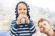 Cute little boy eats delicious hotdog with elder brother on blurry background outdoors. Children dinner with fast food snack on travel. Family time