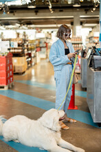 Woman With Her Cute White Dog Visiting Supermarket, Paying On A Cash Register While Her Pet Waiting On Floor