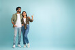 © Prostock-studio - Loving young eastern couple pointing at copy space, colored background