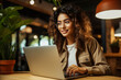 Pretty cheerful Asian woman in eyeglasses casual attire browses laptop connected to 4G internet updates software uses modern technologies and happily poses in a café glancing away 