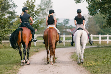 Three horsewomen enjoy riding beautiful horses, side by side along the trail at the equestrian center on a sunny day