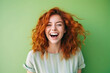 A young beautiful girl with red curly hair and a snow-white smile laughs in green T-shirt on bright green plain background. Human emotions, joy, laughter, happiness