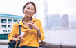 © BullRun - Happy Asian young woman smiling at city embankment