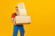 © somemeans - Smiling delivery man or loader holds cartboard boxes on yellow background in studio. Copy space, mock up.