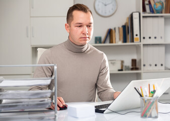 Man office worker sitting at desk and using laptop during his workday.