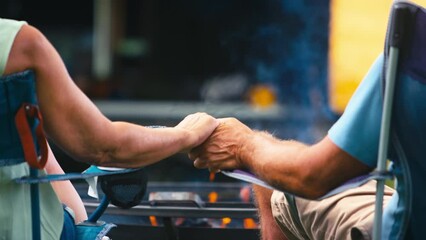 Wall Mural - Rear view of loving senior couple camping in countryside with RV holding hands by outdoor fire - shot in slow motion