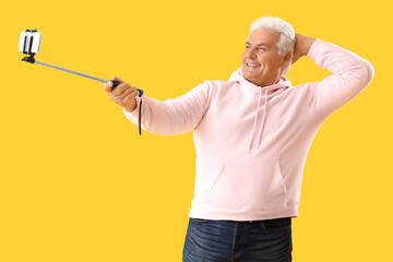 Wall Mural - Senior man with mobile phone taking selfie on yellow background