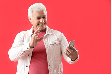 Wall Mural - Senior man with mobile phone video chatting on red background