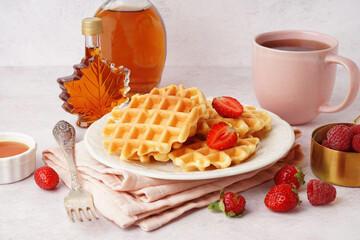 Wall Mural - Tasty waffles with berries, maple syrup and cup of tea on white background