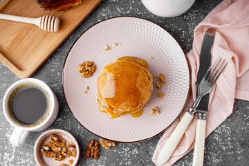 tasty pancakes with nuts, maple syrup and cup of coffee on grey background