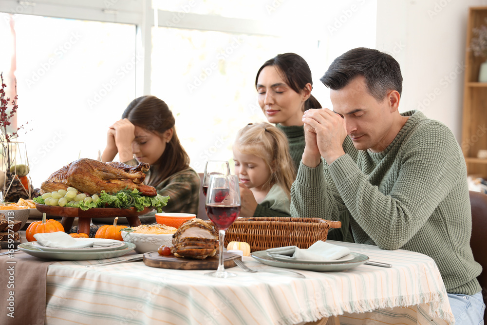 Happy family praying before dinner at festive table on Thanksgiving Day