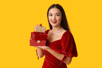 Canvas Print - Beautiful young Asian woman with gift boxes on yellow background