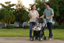 Happy Parent (father And Mother) Talking And Pushing Infant Baby Stroller And Walking In Park