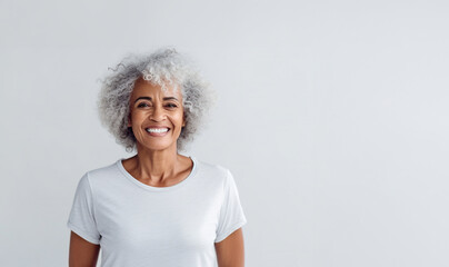 Wall Mural - Portrait of smiling proud handsome african american senior woman standing against isolated white background. Wearing a white t-shirt copy space for advertisement or logo