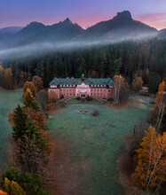 Jetrichovice, Czech Republic - Aerial View Of Beautiful Pink Mansion Near Jetrichovice At Sunrise On A Foggy Autumn Morning With Mariina Vyhlidka Viewpoint At Background In Bohemian Switzerland Region