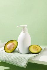 Sticker - Minimalist concept for advertising cosmetic based on avocado extract. A white pump bottle placed on cotton towel with halves of avocado on pastel background. Empty label for design. Front view