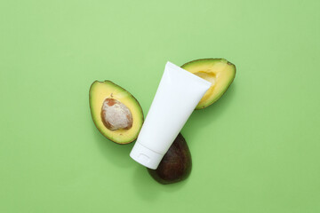 Sticker - Beauty herbal skincare and haircare concept. On a green background, a plastic cosmetic tube decorated with fresh avocado slices. Mockup for packaging design. Advertising photo