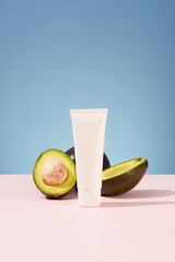 Sticker - Minimalist scene for advertising cosmetic with ingredient from avocado. An empty plastic bottle displayed with fresh halves of avocado on color background. Beauty product design, skincare and haircare