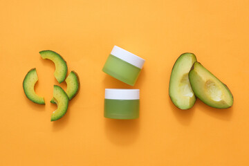 Wall Mural - Beauty product mockup, cosmetics jars decorated with fresh slices of avocado on orange background. Top view, scene for advertising and branding cosmetic with space for design packaging