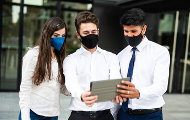 Wall Mural - Business people using a tablet outdoor wearing a protective mask against covid 19 coronavirus pandemic