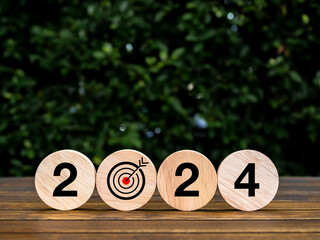 Poster - Happy new year 2024, goal and success with business, environmental sustainability concepts. Target dart icon and 2024 year number on round wooden cube blocks on wood table and green leaves background.