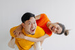 Happy Thai asian couple lover wear orange and yellow, woman riding piggyback on man back. Smiling and laughing, spending time together at apartment, isolated on white background. 