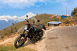 A tourist bike parked on the side of a road at Gumpha Dara View Point with view of the Kanchenjunga Himalaya mountain range near Tinchuley, Darjeeling, India