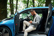 © standret - With smartphone in hands. Beautiful young man is sitting in the blue car outdoors