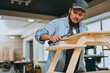 © amixstudio - Carpenter works with wood in carpentry workshop. Man doing woodwork professionally