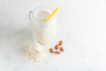 Wall Mural - Glass jar of protein milkshake drink or smoothie and whey protein powder in measuring spoon, almond nuts on a white background. sport nutrition, bodybuilding food supplements