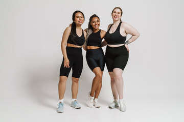 Wall Mural - Three positive women in sportswear hugging isolated over white background