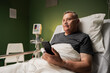 Hospitalized senior gentleman, with a cellphone in hand, resting in bed, while being assisted by an oxygen tube and finger oxygen monitor