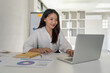 © Natee Meepian - Portrait of beautiful young businesswoman asian sitting at office modern work station and typing on laptop