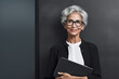 © Surachetsh - The portrait of an old businesswoman in a neatly suit outfit standing and smiling in a modern office, Generative AI.