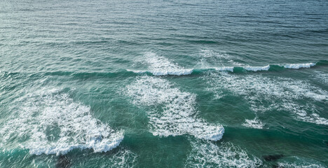 Wall Mural - ocean foamy waves approaching rocky shore. top view.