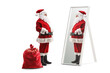 Full length profile shot of santa claus standing next to his sack and looking at a mirror