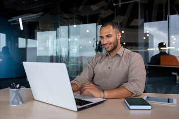 Young successful businessman working inside the office with a laptop, satisfied with the results of the achievement, the man is smiling, typing on the keyboard.