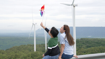 Sticker - Progressive happy mother and her son at the wind turbine farm. Electric generator from wind by wind turbine generator on the country side with hill and mountain on the horizon.