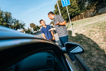Wall Mural - A driving instructor and a student are standing outside next to the car after a driving lesson. The instructor explains to him where he made mistakes.