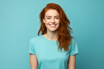 Poster - Smiling Portrait of a Beautiful Fictional Young Woman Wearing Blank Cyan T-Shirt. Isolated on a Plain Blue Colored Background. Generative AI. 