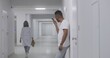 © Framestock - African American man stands in hospital corridor, records voice message and chats by mobile phone. Recovering patient during treatment in modern clinic. Medical staff walk in background. Slow motion.