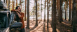 © Anna - A young man stands next to a car with an upper tourist trunk in a pine forest on the shore of a lake at sunset.