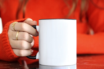 Wall Mural - Girl is holding black handle white 11 oz mug in hands with orange sweater. Blank ceramic cup
