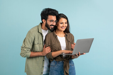 Poster - Loving eastern couple using laptop on plain blue background