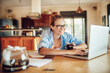 © Geber86 - Happy young woman using her laptop in the kitchen at home